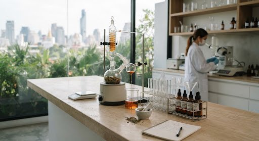 Minimalist laboratory in Bangkok featuring botanical distillation glass equipment and modern skincare research tubes on warm limestone counters under gentle natural light.